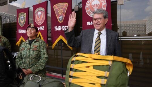 Ricardo Monreal saluda junto a una militar y equipo de paracaidismo durante una exhibición.
